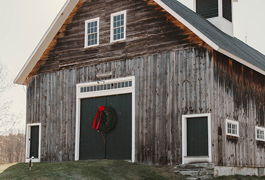 a barn on a grassy hill with a wreath on the front